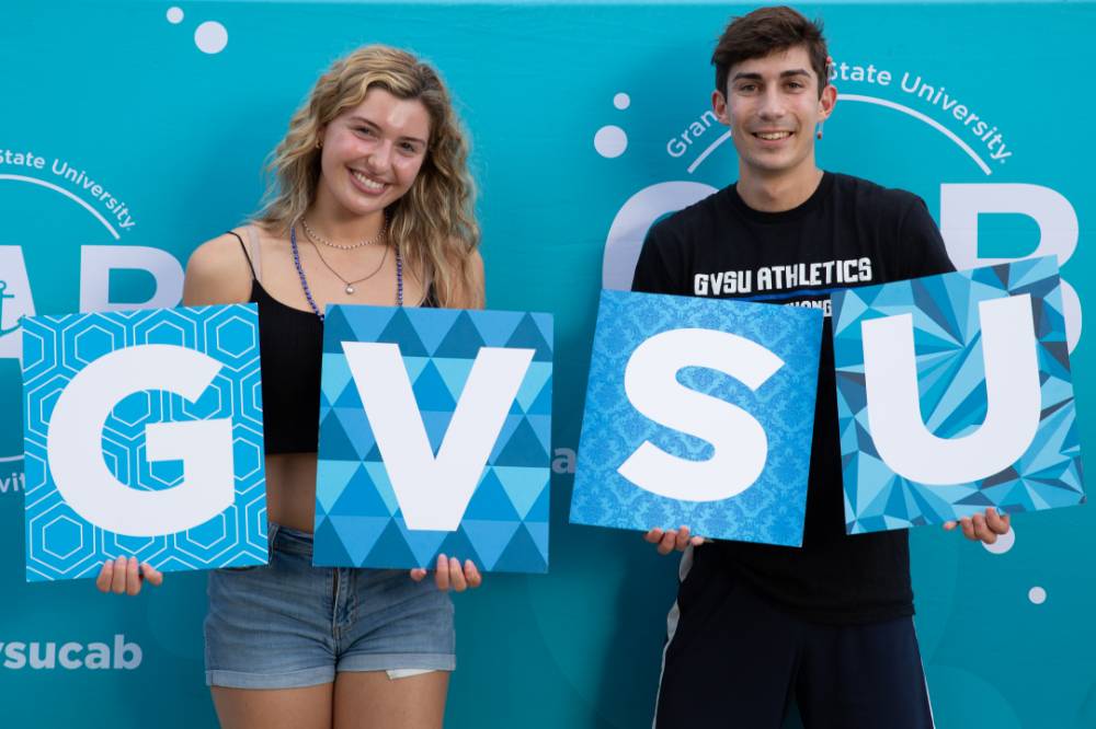 two students posing in front of CAB backdrop at Laker Kickoff photo booth holding GVSU letters
